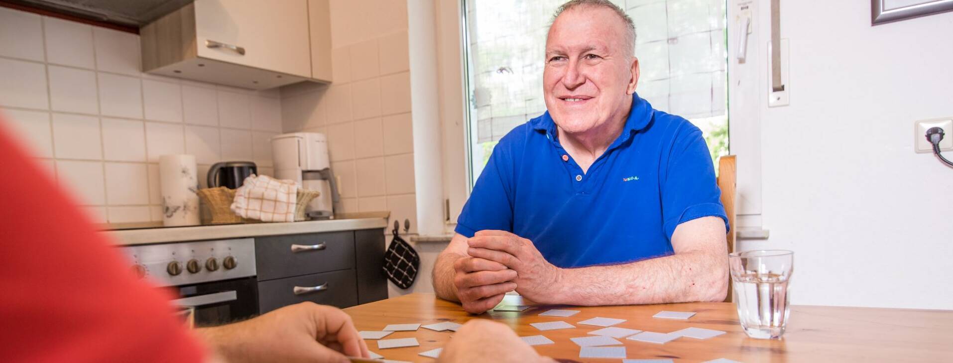 Alter Mann wird beim Kartenspielen gezeigt, und lächelt fröhlich.